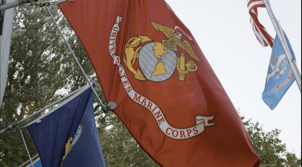 A close-up view of the United States Marine Corps flag waving in the wind, with other flags in the background.
