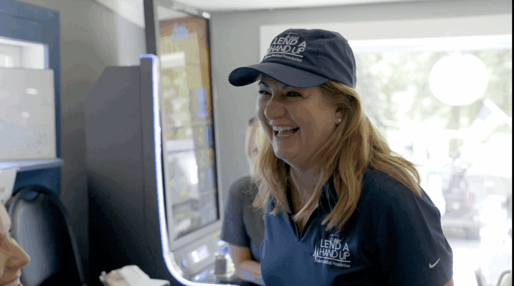 Woman smiling while wearing Lend A Hand Up cap and shirt at indoor event in Fargo