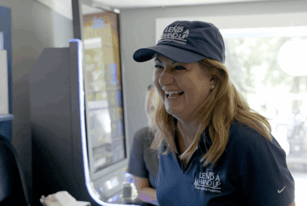 Woman smiling while wearing Lend A Hand Up cap and shirt at indoor event in Fargo